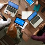 Diverse team discussing business strategies with laptops and tablets at a wooden table.