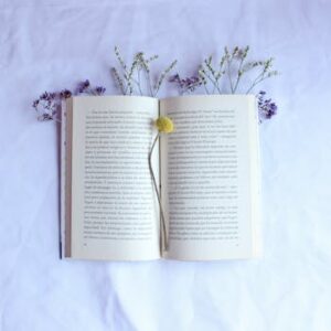 Artistic flat lay of an open book surrounded by delicate flowers on a white surface.